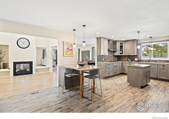 40 Walter Way, Broomfield, CO 80020 - kitchen with wall chimney range hood, light wood-style flooring, glass insert cabinets, tasteful backsplash, and light stone countertops