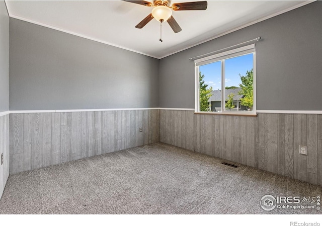 2217 Waylon Dr, Johnstown, CO 80534 - empty room featuring ceiling fan, wainscoting, carpet floors, wood walls, and ornamental molding