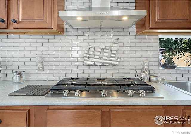2036 1st Ave Unit 437, Greeley, CO 80631 - kitchen view of extractor fan, stainless steel gas cooktop, backsplash, brown cabinetry, and light countertops