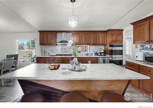 2036 1st Ave Unit 437, Greeley, CO 80631 - kitchen featuring stainless steel appliances, wall chimney range hood, a breakfast bar area, wood finished floors, and brown cabinets