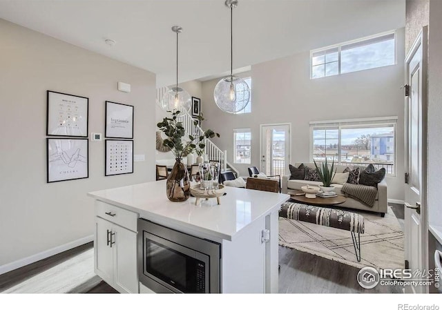 921 Abbott Ln, Fort Collins, CO 80524 - kitchen with stainless steel microwave, light wood-type flooring, white cabinetry, decorative light fixtures, and a high ceiling