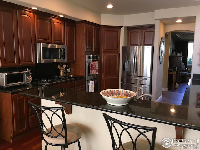 1402 Westfield Dr, Fort Collins, CO 80526 - kitchen with appliances with stainless steel finishes, arched walkways, a kitchen breakfast bar, dark stone countertops, and tasteful backsplash