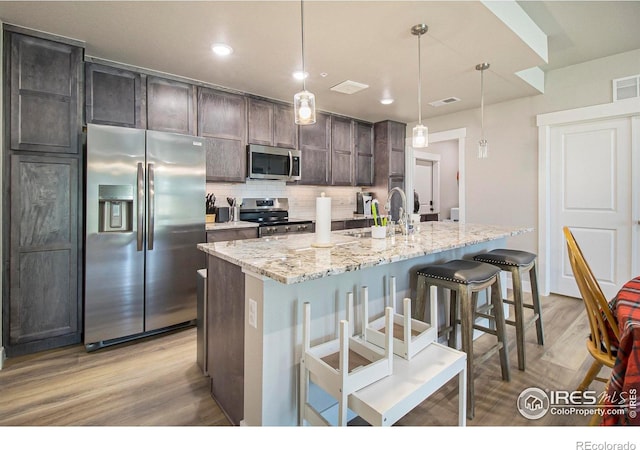 285 High Point Dr Unit H-104, Longmont, CO 80504 - kitchen featuring stainless steel appliances, light wood finished floors, backsplash, light stone counters, and an island with sink