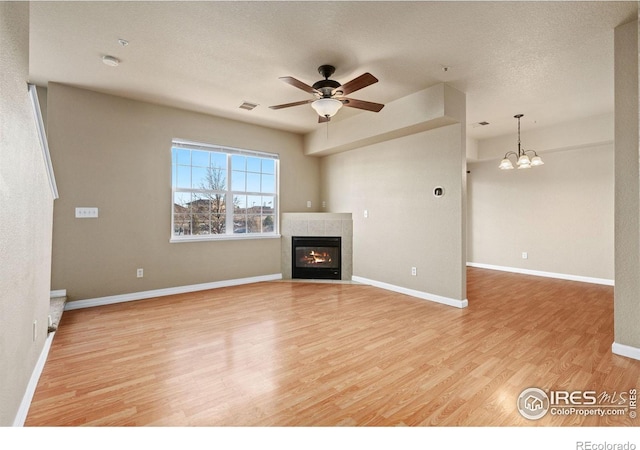 6925 19th St Unit 15, Greeley, CO 80634 - unfurnished living room with light wood-type flooring, a ceiling fan, a tile fireplace, and a chandelier