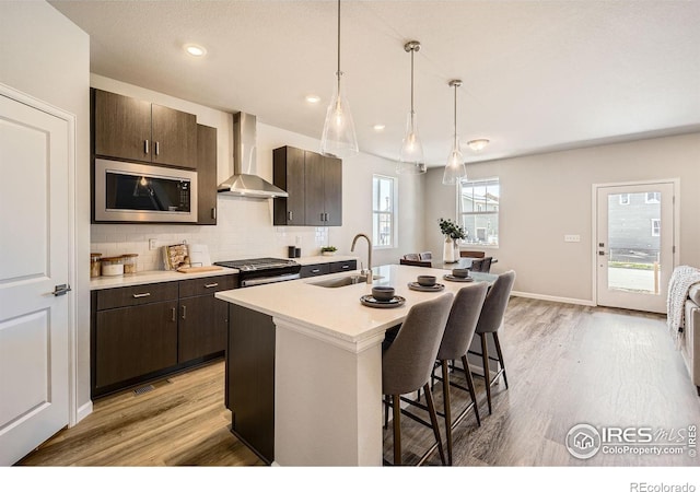 2290 Walbridge Rd, Fort Collins, CO 80524 - kitchen featuring wall chimney range hood, stainless steel microwave, a breakfast bar, dark brown cabinets, and light countertops