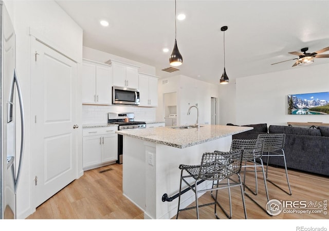 9873 Ceylon St, Commerce City, CO 80022 - kitchen featuring appliances with stainless steel finishes, open floor plan, light wood finished floors, tasteful backsplash, and white cabinets