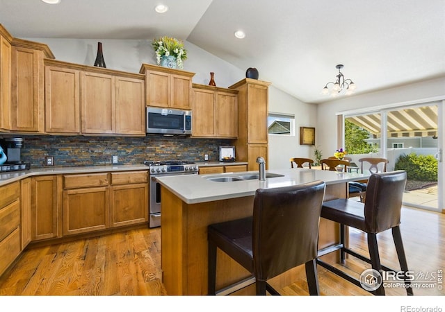 1613 Alpine Ave, Berthoud, CO 80513 - kitchen with stainless steel appliances, vaulted ceiling, a breakfast bar area, decorative backsplash, and light wood finished floors