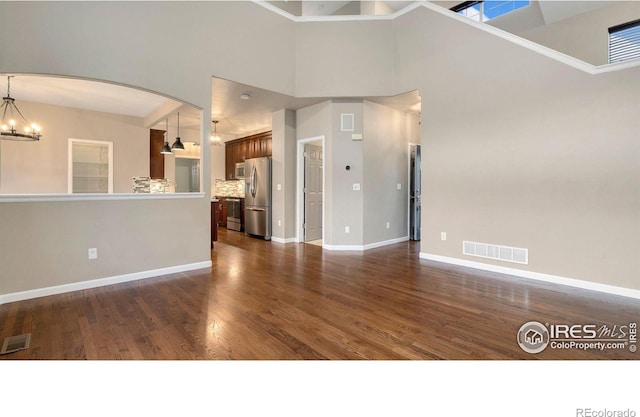 1937 Mahogany Way, Severance, CO 80550 - unfurnished living room featuring a chandelier, dark wood-type flooring, arched walkways, and a towering ceiling