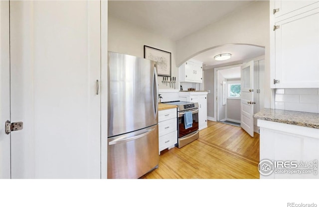 5326 Lowell Blvd, Denver, CO 80221 - kitchen with stainless steel appliances, arched walkways, light wood-style floors, white cabinets, and tasteful backsplash