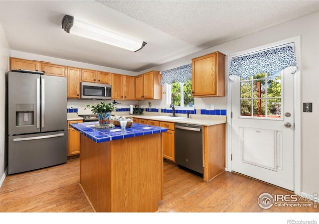 1026 Red Oak Dr, Longmont, CO 80504 - kitchen with stainless steel appliances, tile countertops, a center island, light wood-style floors, and a textured ceiling