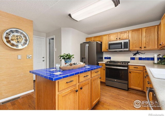 1026 Red Oak Dr, Longmont, CO 80504 - kitchen featuring stainless steel appliances, tile countertops, light wood-style floors, a kitchen island, and a textured ceiling