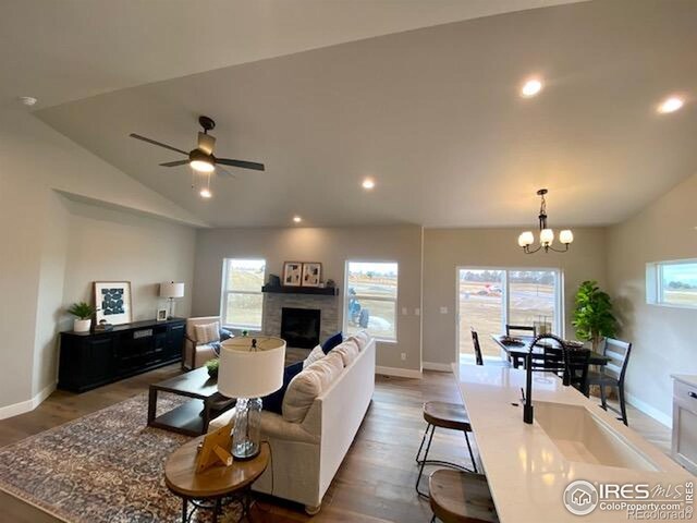 7156 Feather Reed Dr, Wellington, CO 80549 - living area with plenty of natural light, vaulted ceiling, a fireplace, wood finished floors, and a chandelier