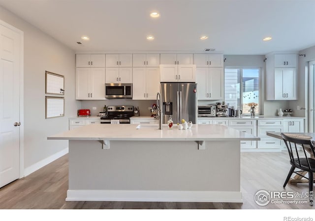 6645 Dry Fork Dr, Frederick, CO 80516 - kitchen with stainless steel appliances, a kitchen breakfast bar, white cabinetry, light wood-style floors, and recessed lighting