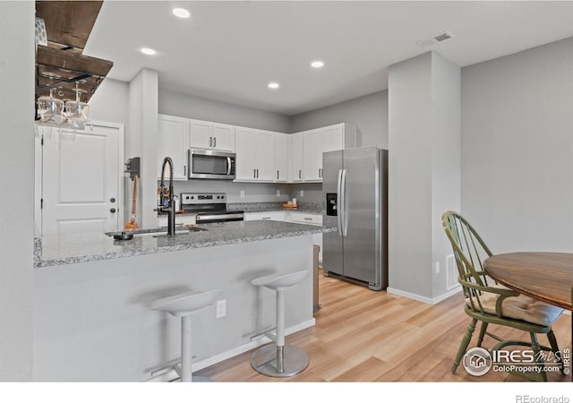3644 Ronald Reagan Ave, Wellington, CO 80549 - kitchen featuring appliances with stainless steel finishes, light wood-type flooring, white cabinetry, light stone countertops, and a peninsula