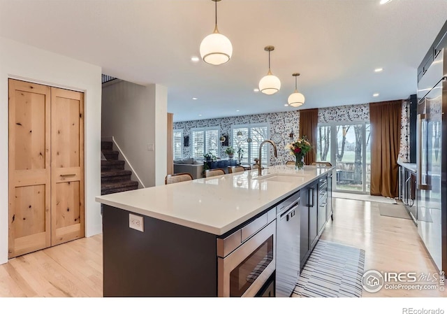 1405 Clover Creek Dr, Longmont, CO 80503 - kitchen with appliances with stainless steel finishes, light wood-type flooring, a kitchen island with sink, decorative light fixtures, and light countertops