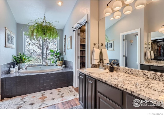 1405 Clover Creek Dr, Longmont, CO 80503 - bathroom with vanity, a garden tub, vaulted ceiling, wood finished floors, and a spacious closet