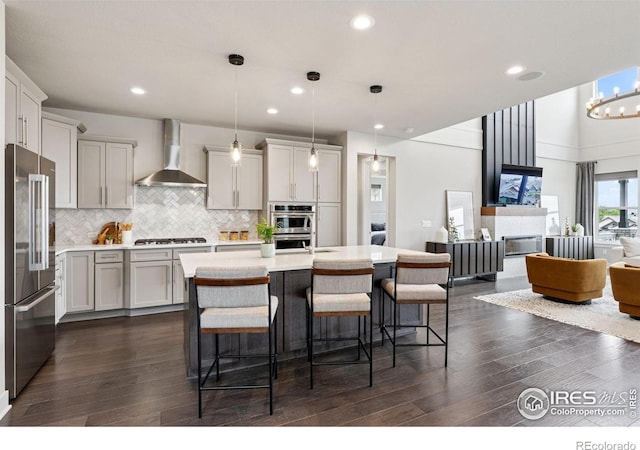 3315 Heron Lakes Pkwy, Berthoud, CO 80513 - kitchen with wall chimney range hood, stainless steel appliances, dark wood finished floors, light countertops, and tasteful backsplash