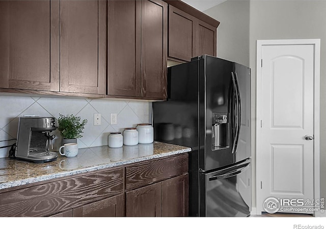 1384 S Growers Dr, Milliken, CO 80543 - kitchen featuring black fridge, dark brown cabinets, tasteful backsplash, and light stone countertops