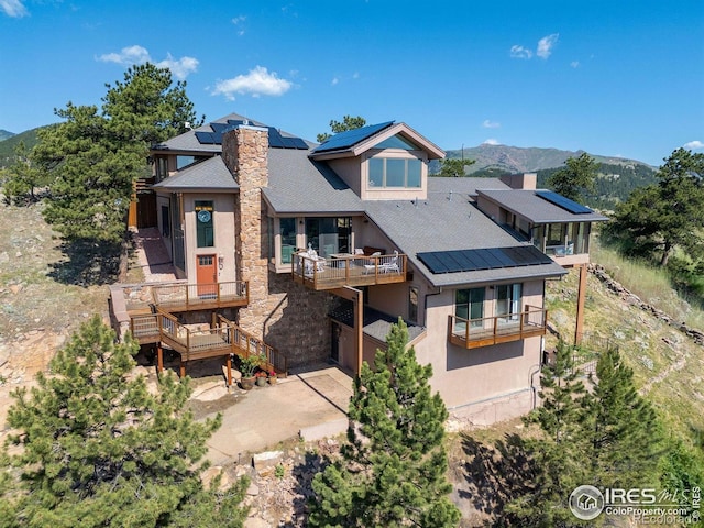 6183 Red Hill Rd, Boulder, CO 80302 - rear view of house with roof mounted solar panels, stucco siding, a chimney, a balcony, and stone siding