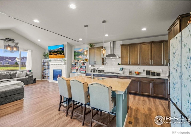 437 Buckskin Rd, Berthoud, CO 80513 - kitchen with wall chimney exhaust hood, stainless steel gas cooktop, light wood-style floors, a kitchen breakfast bar, and tasteful backsplash