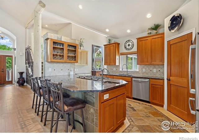 4926 Saint Andrews Ct, Loveland, CO 80537 - kitchen featuring stainless steel appliances, a kitchen breakfast bar, dark stone counters, brown cabinets, and glass insert cabinets