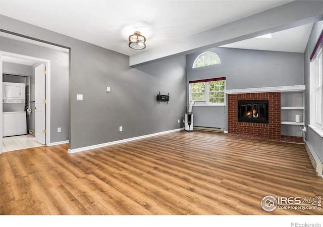 3531 Windmill Dr Unit 3, Fort Collins, CO 80526 - unfurnished living room with estacked washer and dryer, light wood-type flooring, lofted ceiling, a fireplace, and a baseboard radiator