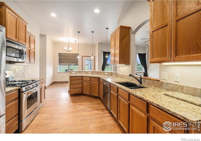20199 Leola Way, Eaton, CO 80615 - kitchen with appliances with stainless steel finishes, light wood-type flooring, brown cabinetry, a peninsula, and light stone counters