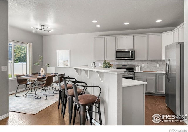 5612 Osbourne Dr, Windsor, CO 80550 - kitchen with appliances with stainless steel finishes, a kitchen bar, light countertops, dark wood-type flooring, and recessed lighting
