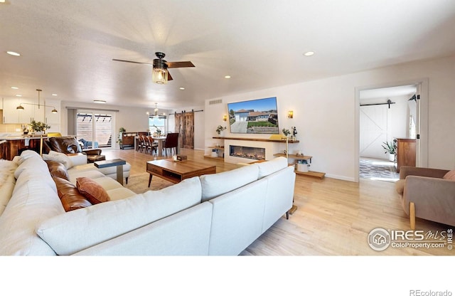1403 Crestridge Dr, Loveland, CO 80537 - living room with light wood finished floors, a barn door, a ceiling fan, recessed lighting, and a glass covered fireplace