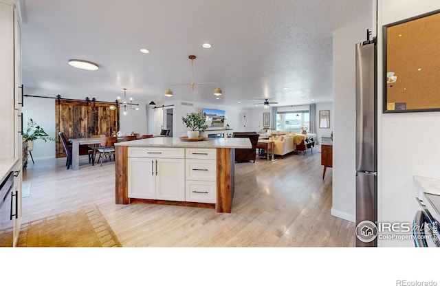 1403 Crestridge Dr, Loveland, CO 80537 - kitchen with a barn door, open floor plan, white cabinetry, light wood-type flooring, and freestanding refrigerator