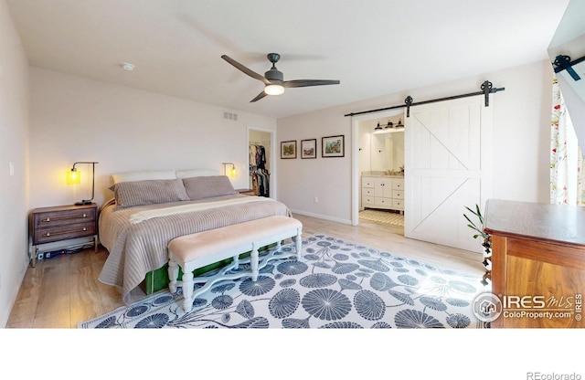 1403 Crestridge Dr, Loveland, CO 80537 - bedroom with a barn door, light wood finished floors, a spacious closet, a ceiling fan, and connected bathroom