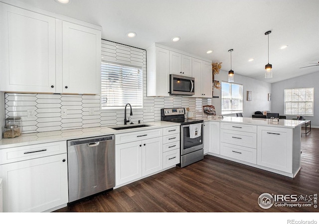 3536 38th Ave, Evans, CO 80620 - kitchen with appliances with stainless steel finishes, a peninsula, dark wood-type flooring, white cabinetry, and decorative backsplash