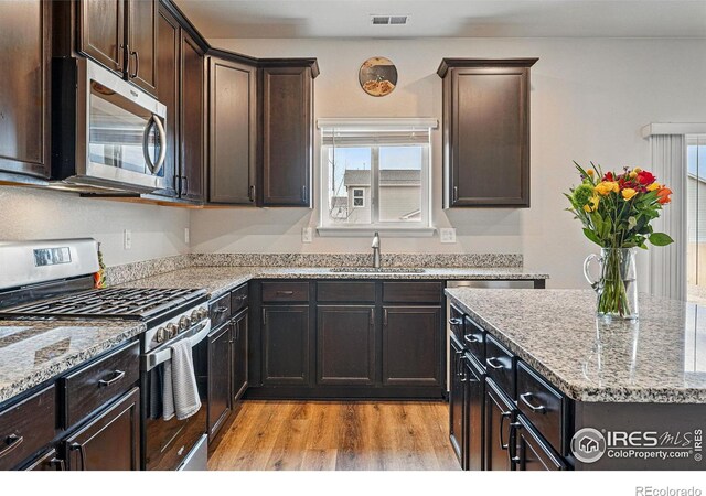 2310 Angus St, Mead, CO 80542 - kitchen featuring appliances with stainless steel finishes, light wood-type flooring, light stone counters, and dark brown cabinets