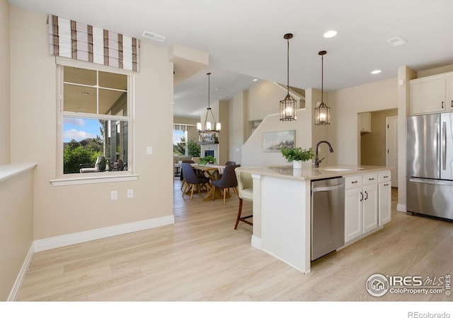 2599 Trio Falls Dr, Loveland, CO 80538 - kitchen with stainless steel appliances, a chandelier, light wood-type flooring, white cabinetry, and an island with sink