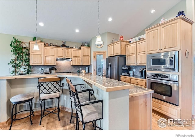 9629 Bountiful St, Firestone, CO 80504 - kitchen featuring appliances with stainless steel finishes, light brown cabinets, under cabinet range hood, a breakfast bar area, and vaulted ceiling