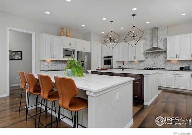 15958 Humboldt Peak Dr, Broomfield, CO 80023 - kitchen featuring wall chimney exhaust hood, a kitchen island with sink, appliances with stainless steel finishes, tasteful backsplash, and dark wood-style flooring