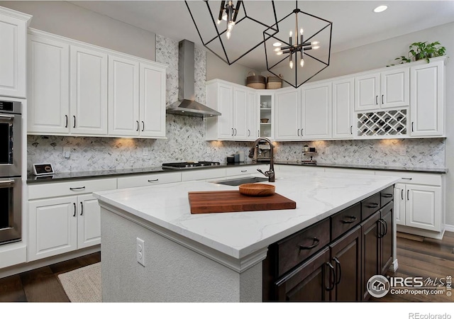 15958 Humboldt Peak Dr, Broomfield, CO 80023 - kitchen with wall chimney exhaust hood, white cabinetry, decorative backsplash, a chandelier, and dark wood-style floors
