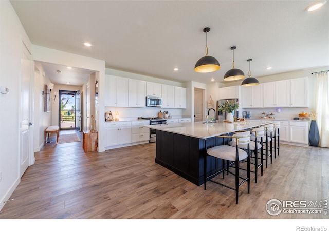 4918 Preserve Pl, Firestone, CO 80504 - kitchen featuring appliances with stainless steel finishes, light wood-type flooring, recessed lighting, white cabinetry, and a kitchen bar