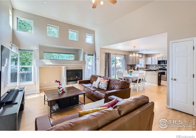 1747 Daisy Ct, Brighton, CO 80601 - living area featuring a high ceiling, light wood-type flooring, ceiling fan, a chandelier, and a tiled fireplace