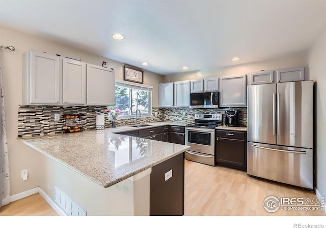 1747 Daisy Ct, Brighton, CO 80601 - kitchen featuring stainless steel appliances, a peninsula, light stone countertops, light wood-type flooring, and backsplash