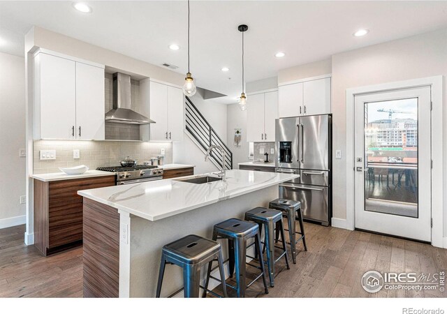 3450 N Downing St Unit 4, Denver, CO 80205 - kitchen with stainless steel appliances, wall chimney range hood, light wood-type flooring, a kitchen breakfast bar, and decorative backsplash