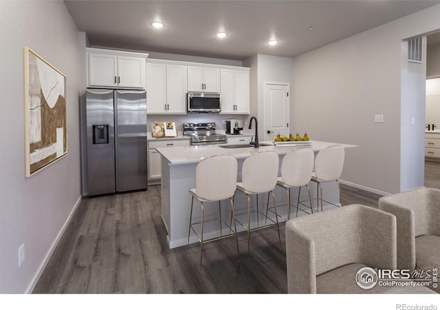 2714 Barnstormer St Unit G, Fort Collins, CO 80524 - kitchen featuring appliances with stainless steel finishes, a kitchen island with sink, dark wood-style flooring, a kitchen breakfast bar, and white cabinets