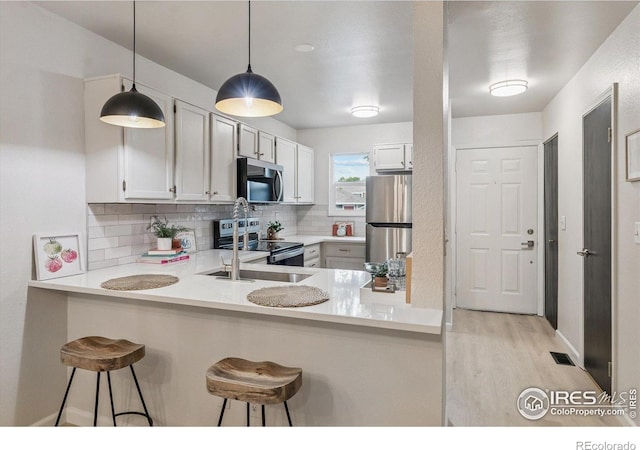 7474 E Arkansas Ave Unit 12, Denver, CO 80231 - kitchen featuring appliances with stainless steel finishes, decorative backsplash, light wood-type flooring, a kitchen bar, and a peninsula