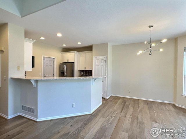 3000 E 112th Ave Unit 102, Northglenn, CO 80233 - kitchen with stainless steel fridge, wood finished floors, white cabinets, a chandelier, and recessed lighting