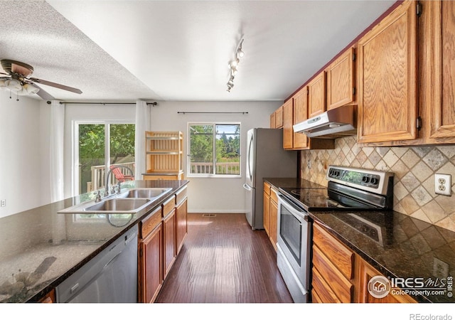 1305 Inverness Dr, Lafayette, CO 80026 - kitchen featuring under cabinet range hood, appliances with stainless steel finishes, dark wood-style flooring, backsplash, and brown cabinetry