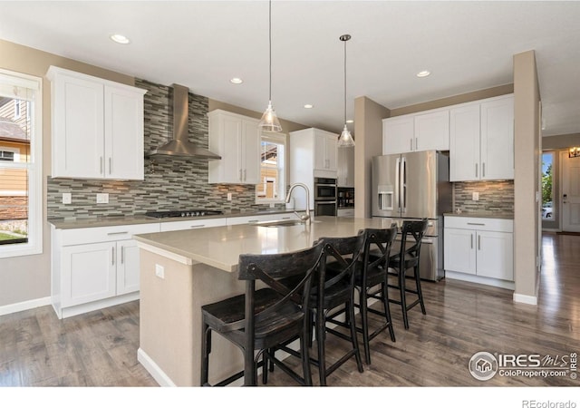 8541 Allenbrook Dr, Windsor, CO 80550 - kitchen with appliances with stainless steel finishes, wall chimney exhaust hood, backsplash, wood finished floors, and a center island with sink