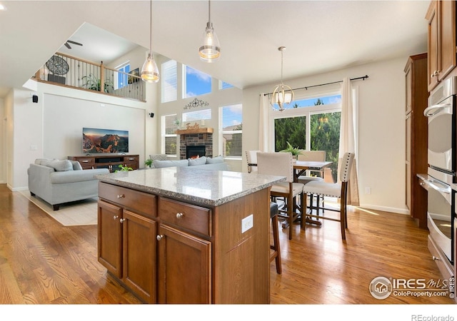 5355 Brookline Dr, Timnath, CO 80547 - kitchen featuring brown cabinets, wood finished floors, hanging light fixtures, a stone fireplace, and a towering ceiling