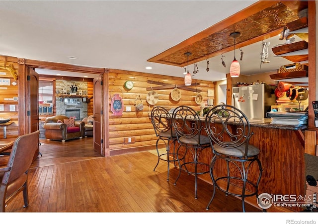 2238 Eagle Cliff Rd, Estes Park, CO 80517 - kitchen with rustic walls, hardwood / wood-style flooring, freestanding refrigerator, a breakfast bar area, and a fireplace