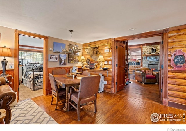 2238 Eagle Cliff Rd, Estes Park, CO 80517 - dining space with wood-type flooring, a chandelier, a stone fireplace, wainscoting, and wooden walls