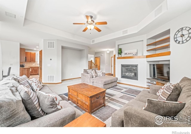 502 Peregrine Cir, Longmont, CO 80504 - living area featuring a raised ceiling, a ceiling fan, a glass covered fireplace, and built in features